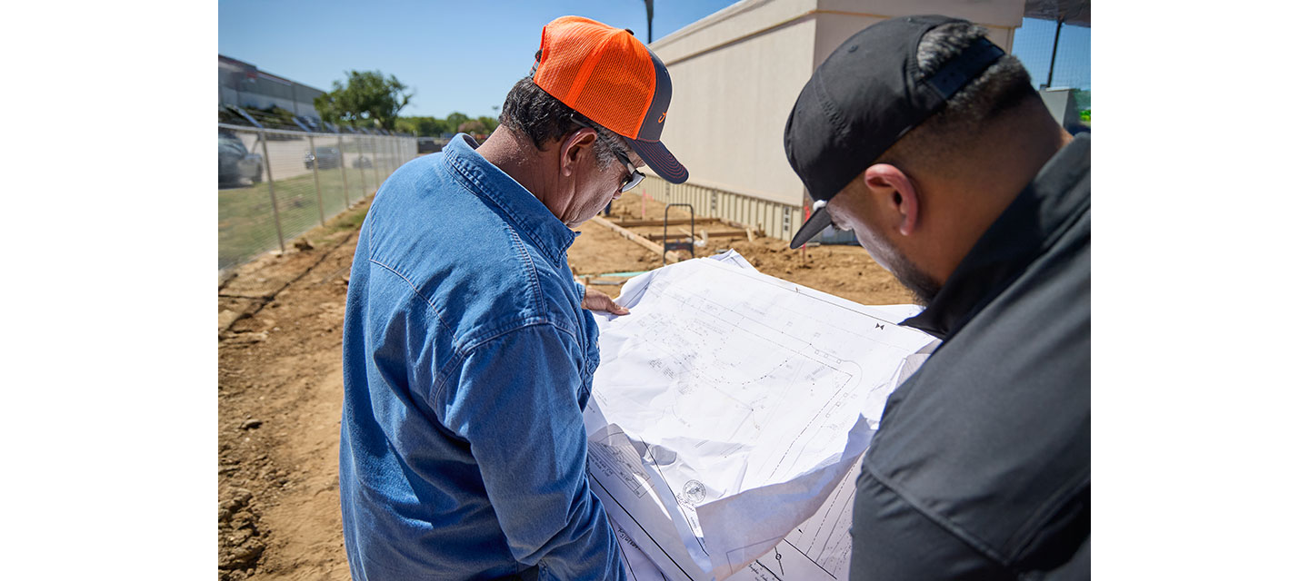 Two men, Benny and Leno Aguilar, review a large set of construction blueprints.